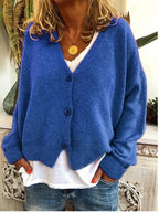 Blue knitted cardigan with button placket and dropped shoulders, layered over white top and denim