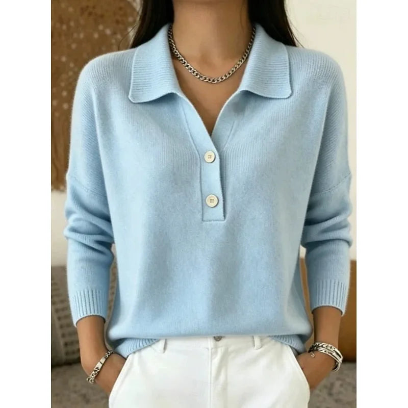 Close-up of a light blue knitted polo jumper with collar, two buttons and dropped shoulders, worn with white trousers.