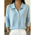Close-up of a light blue knitted polo jumper with collar, two buttons and dropped shoulders, worn with white trousers.