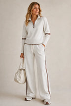 Woman wearing an oatmeal marl quarter-zip jumper and wide-leg trousers with brown stripe trim and white trainers
