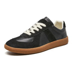 Angled side view of black leather and suede trainers with cream laces and a gum sole on a white background