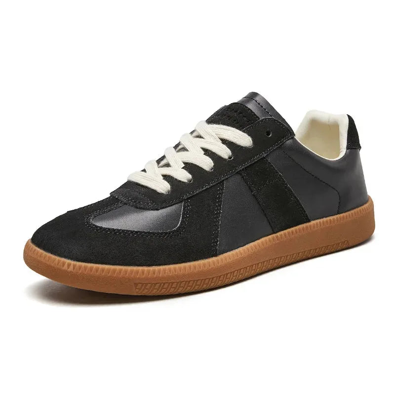Angled side view of black leather and suede trainers with cream laces and a gum sole on a white background