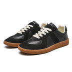 Side view pair of black leather and suede trainers against a plain white background highlighting the gum outsole