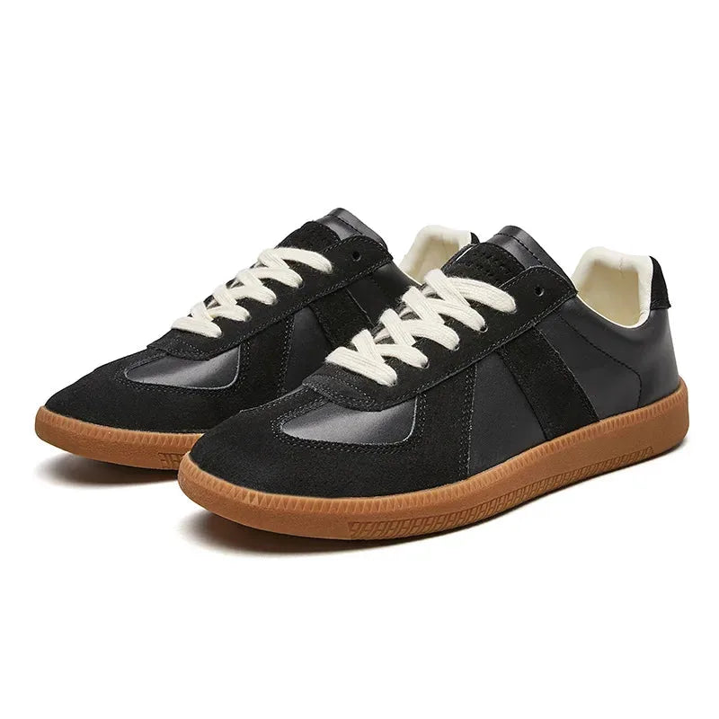Side view pair of black leather and suede trainers against a plain white background highlighting the gum outsole