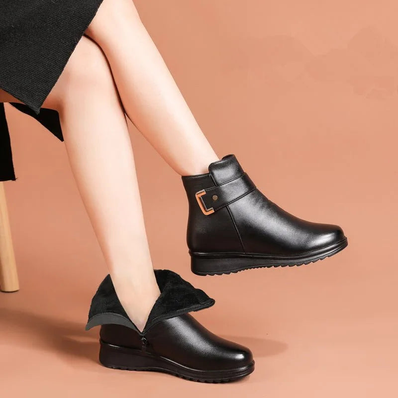 Woman's legs crossed wearing black leather ankle boots with buckle strap and low wedge, one boot folded to show fur lining