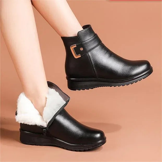 Close-up of black leather ankle boots on a model, showing rounded toe, buckle trim and folded fleece collar