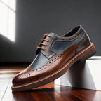 Side profile of a brown, navy and grey wingtip brogue derby shoe with tan laces, resting against a white block