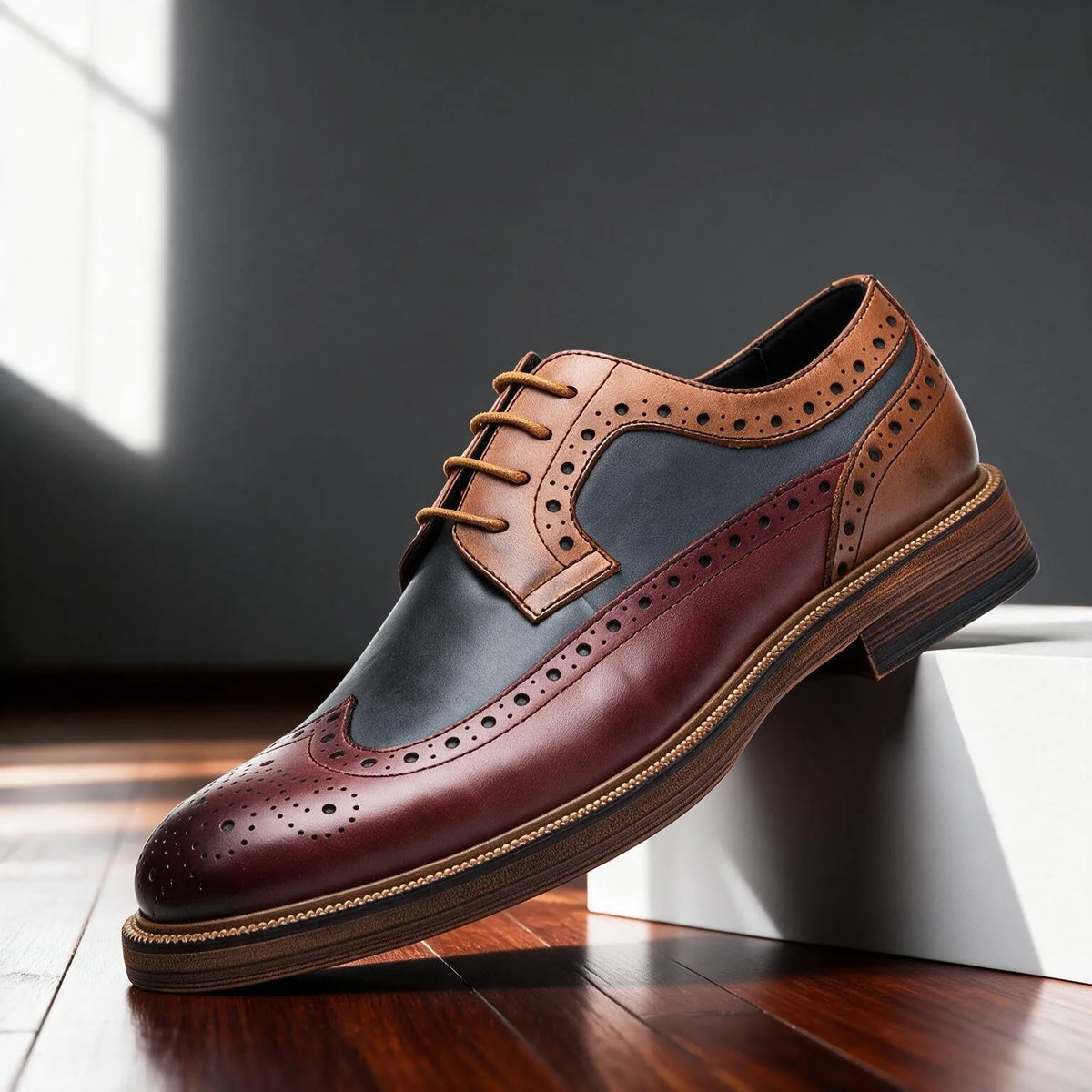 Burgundy, navy and tan wingtip brogue derby shoe shown in side profile with tan laces on a wooden floor
