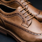 Macro shot of tan brown brogue derby shoes highlighting the waxed laces and pinhole detailing
