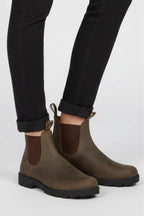 Side view of both feet wearing brown Chelsea boots with dark elastic gussets and stacked sole