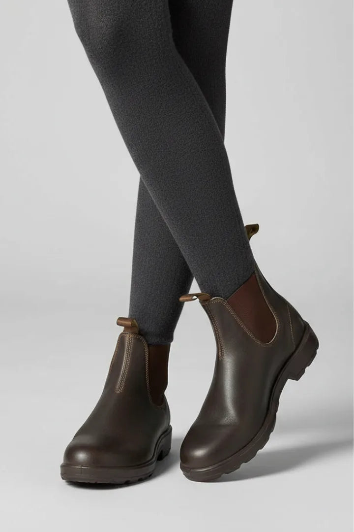 Side profile of a person crossing legs in grey tights wearing dark brown Chelsea boots