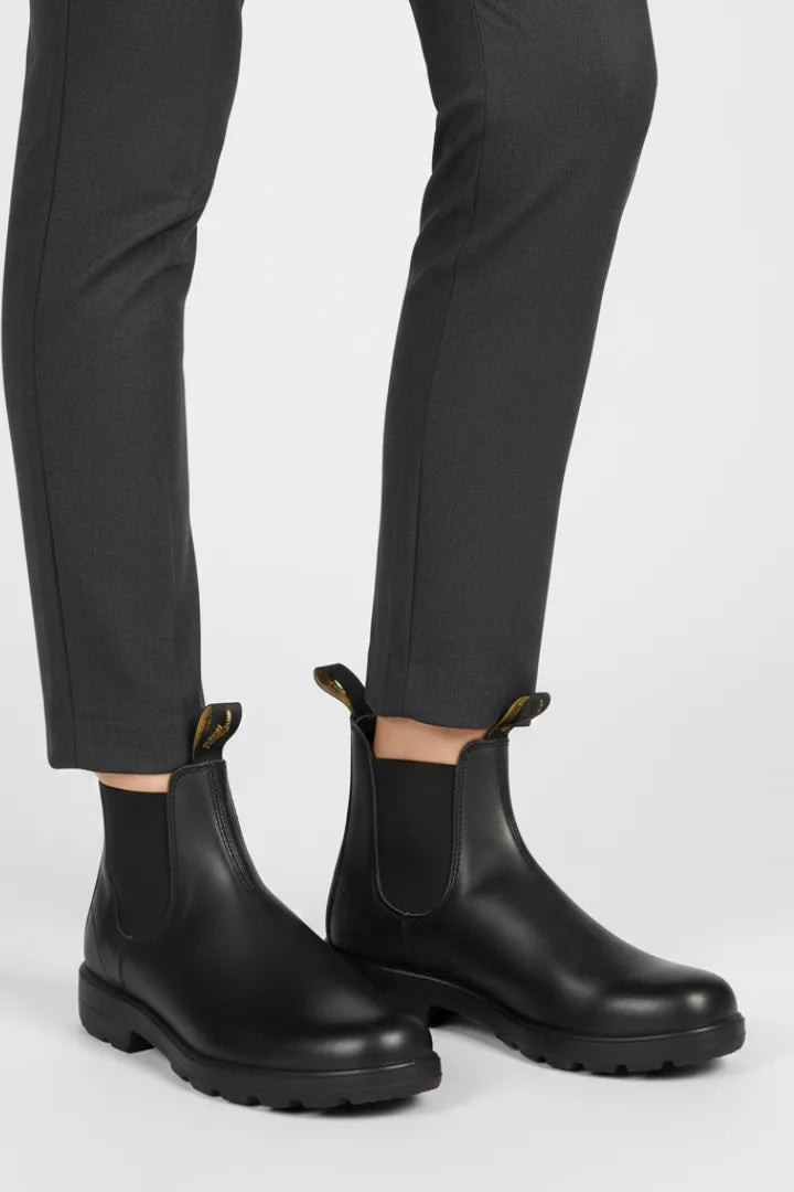 Close-up of black leather Chelsea boots with matching elastic panels worn with grey tailored trousers