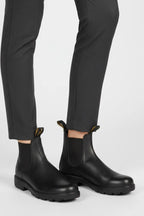 Close-up of black leather Chelsea boots with matching elastic panels worn with grey tailored trousers