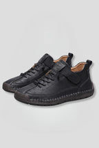 Angled front view of black leather trainers with lace-up front, elastic strap and hand-stitched detailing around the sole