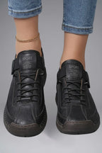 Close-up front view of feet wearing black leather trainers with SPORT branded tongue and adjustable elastic strap