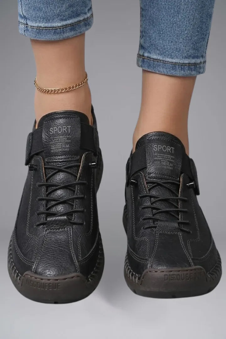 Close-up front view of feet wearing black leather trainers with SPORT branded tongue and adjustable elastic strap
