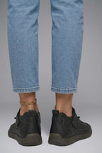 Back heel view of black leather trainers worn with cropped light-wash jeans, showing the pull tab and sole profile