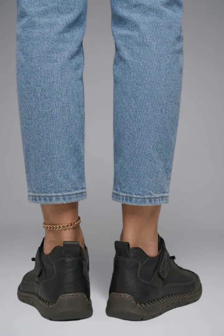 Back heel view of black leather trainers worn with cropped light-wash jeans, showing the pull tab and sole profile