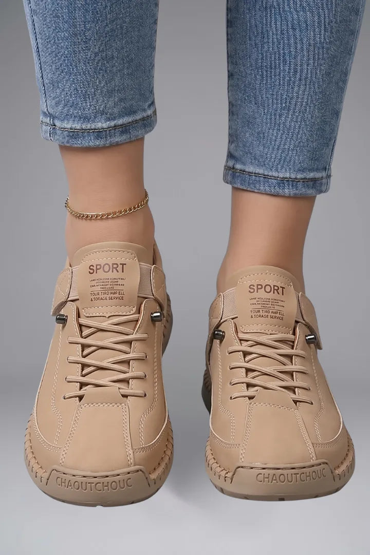 Close-up front view of feet wearing beige leather trainers with SPORT branded tongue and stitched panel detailing