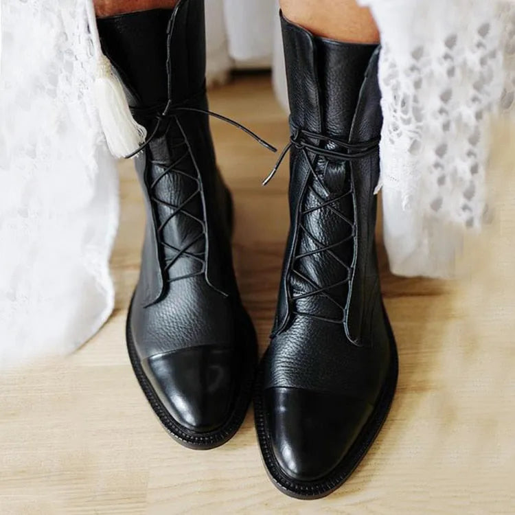 Front view of black leather lace-up boots worn with a white lace dress, glossy cap toe visible