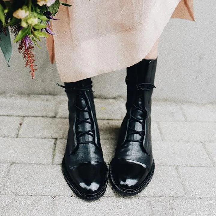 Front view of black leather lace-up boots paired with denim and a black handbag with gold hardware