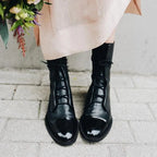 Front view of black leather lace-up boots paired with denim and a black handbag with gold hardware
