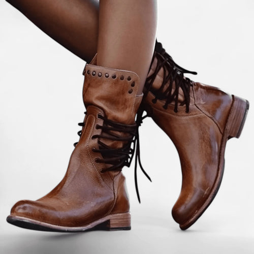 Side view of tan brown leather lace-up boots with stud detailing worn on crossed legs, showing the almond toe shape