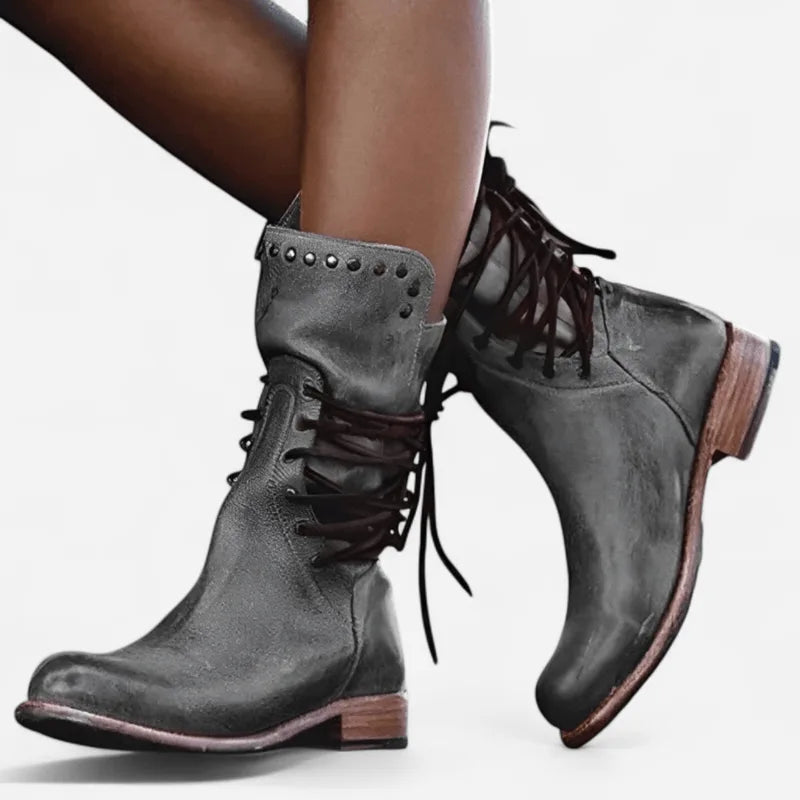 Grey leather lace-up boots with stud detailing shown from the side on crossed legs