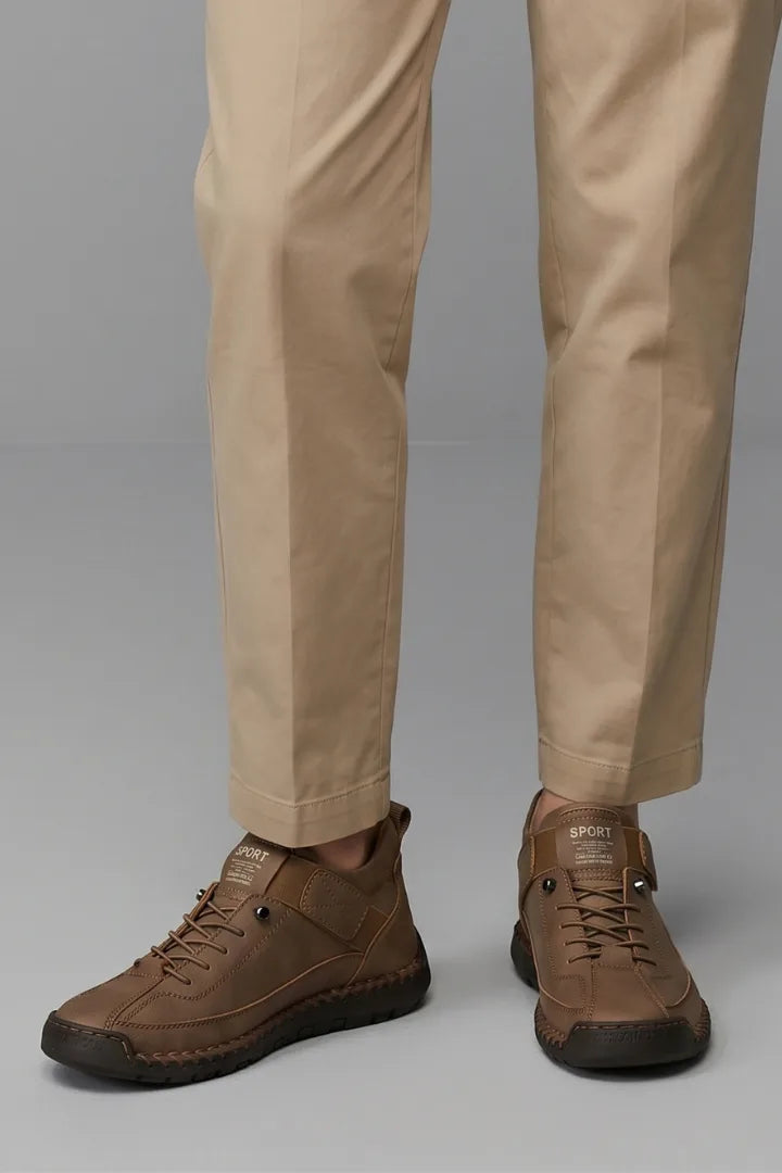Close-up side view of brown leather trainers with hook-and-loop strap worn with beige tapered trousers
