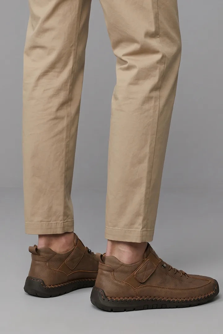 Rear angled view of brown leather trainers showing whipstitched sole and heel pull tab