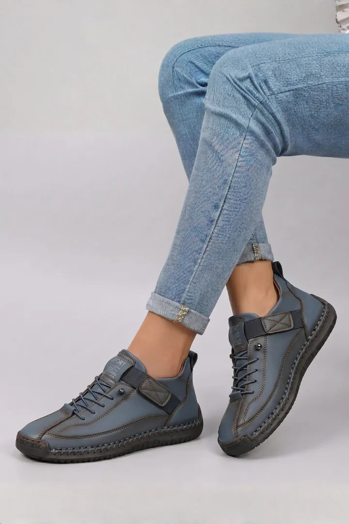 Side view of navy blue leather lace-up trainers worn with rolled-up blue jeans