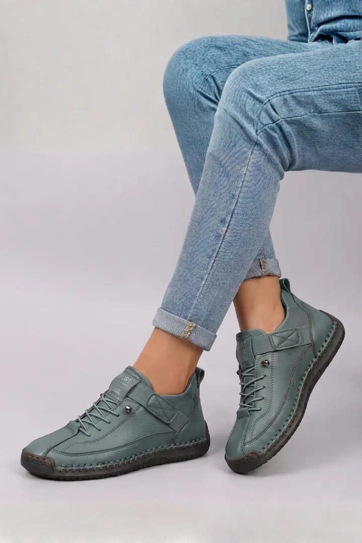 Side view of sage green leather lace-up trainers with stitched welt worn with rolled blue jeans