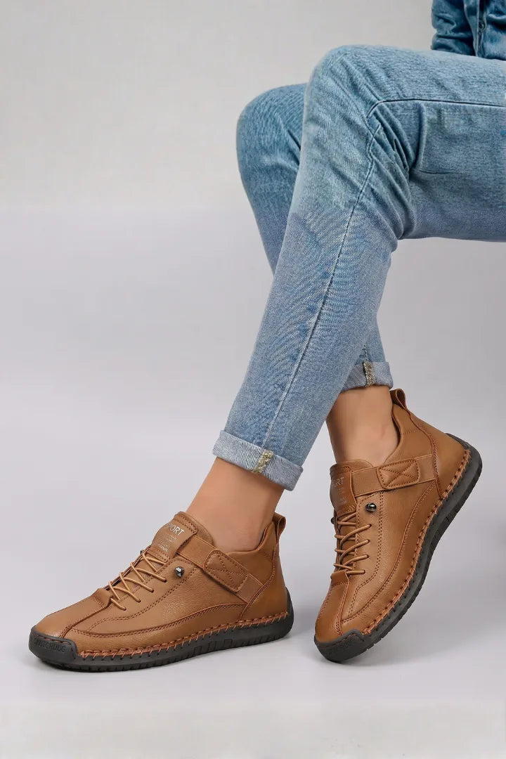 Side view of tan brown leather lace-up trainers with contrast stitching worn with rolled blue jeans