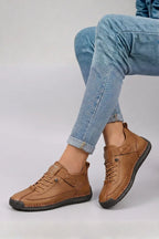 Side view of tan brown leather lace-up trainers with contrast stitching worn with rolled blue jeans
