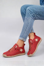 Side view of red leather lace-up trainers with beige strap and stitched sole worn with rolled blue jeans