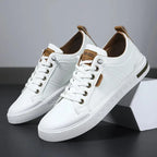 Angled view of white leather trainers with tan heel tab and lace-up front, resting against a white box