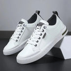 Pair of white trainers with grey heel tab and black eyelets, angled beside a geometric white box