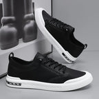Pair of black leather trainers, one upside down showing the patterned white sole and heel pull tab
