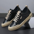 Black leather trainers with cream laces and tan contrast outsole, angled against a white box