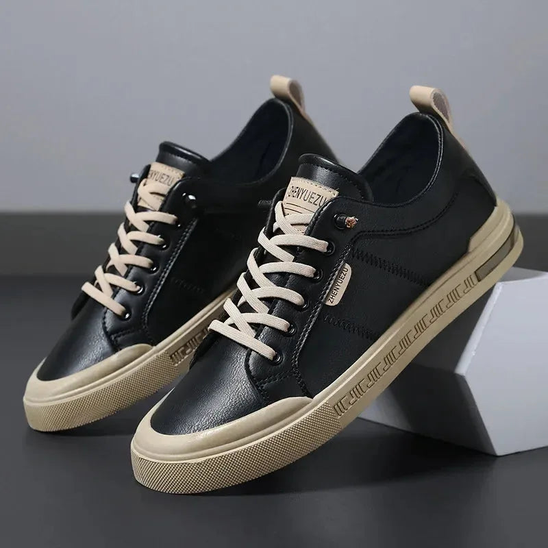 Black leather trainers with cream laces and tan contrast outsole, angled against a white box