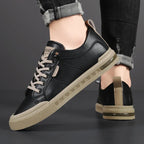 Pair of black leather trainers with cream laces and tan soles viewed from above at an angle
