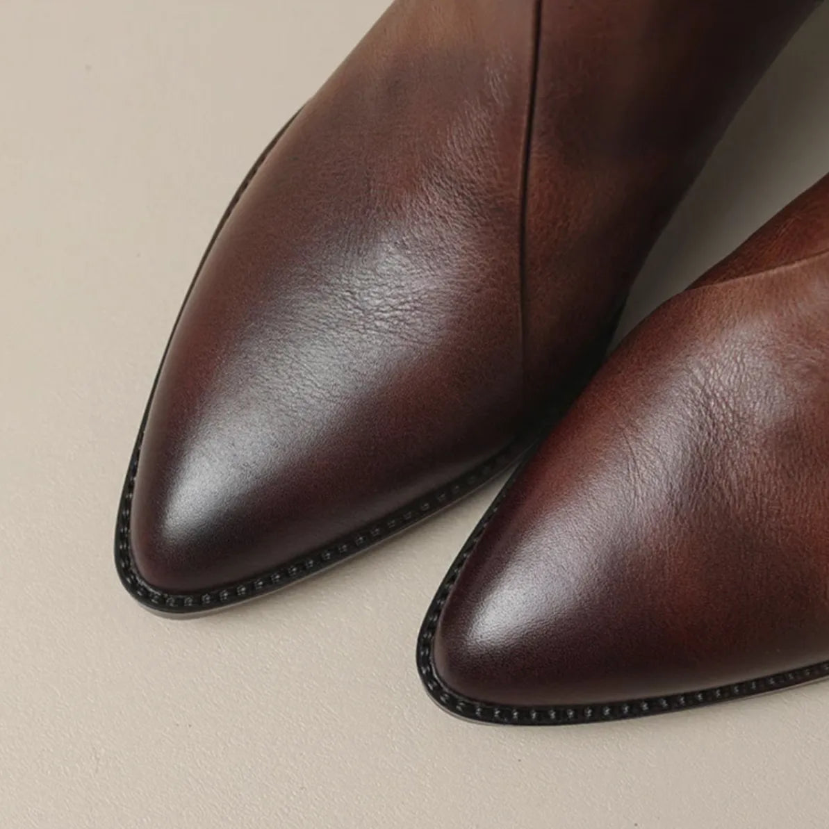 Close-up of brown leather ankle boots showing gold-tone back zip and stacked heel
