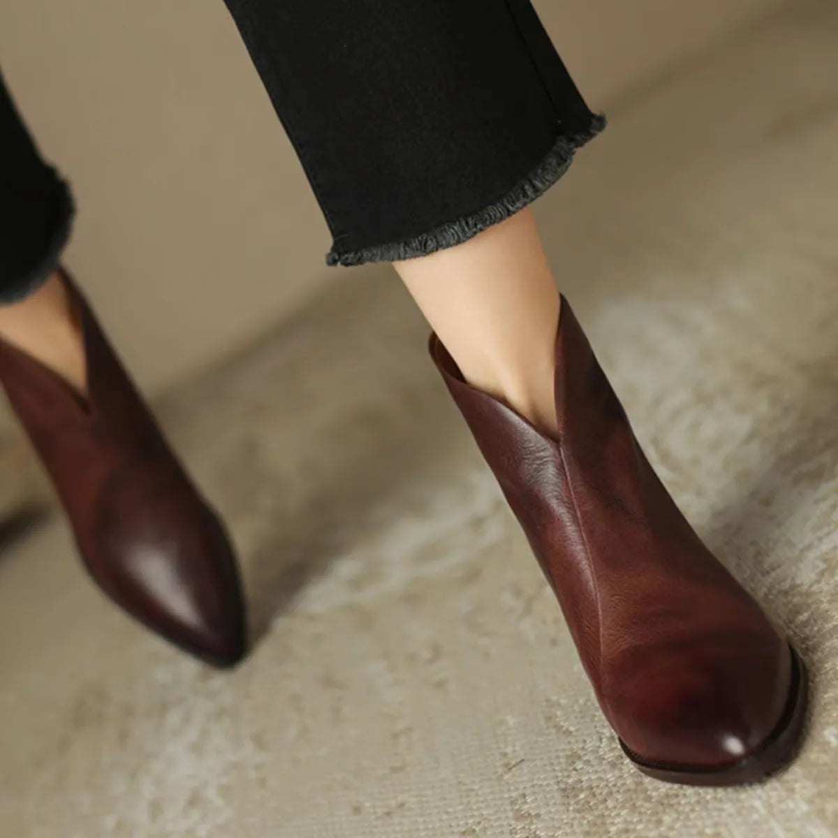 Model walking in burgundy brown leather ankle boots with cropped black trousers