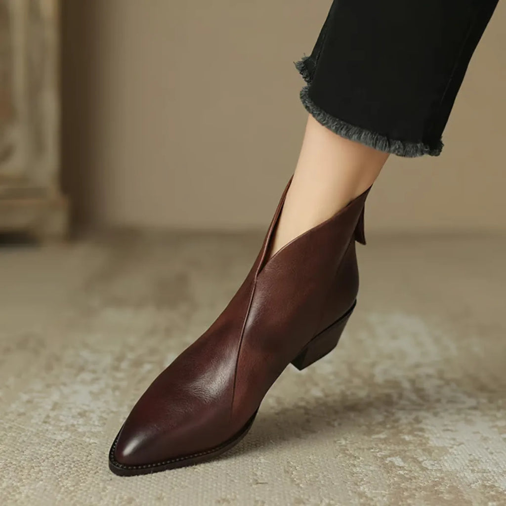 Close-up of burgundy leather ankle boot with V-cut vamp worn with black cropped trousers
