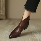 Close-up of burgundy leather ankle boot with V-cut vamp worn with black cropped trousers