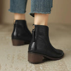 Black leather ankle boot displayed on a woven stool, showing heel height and vamp shape