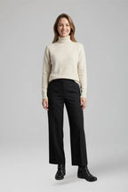 Woman wearing a cream polo neck jumper, black wide-leg trousers and black ruched ankle boots