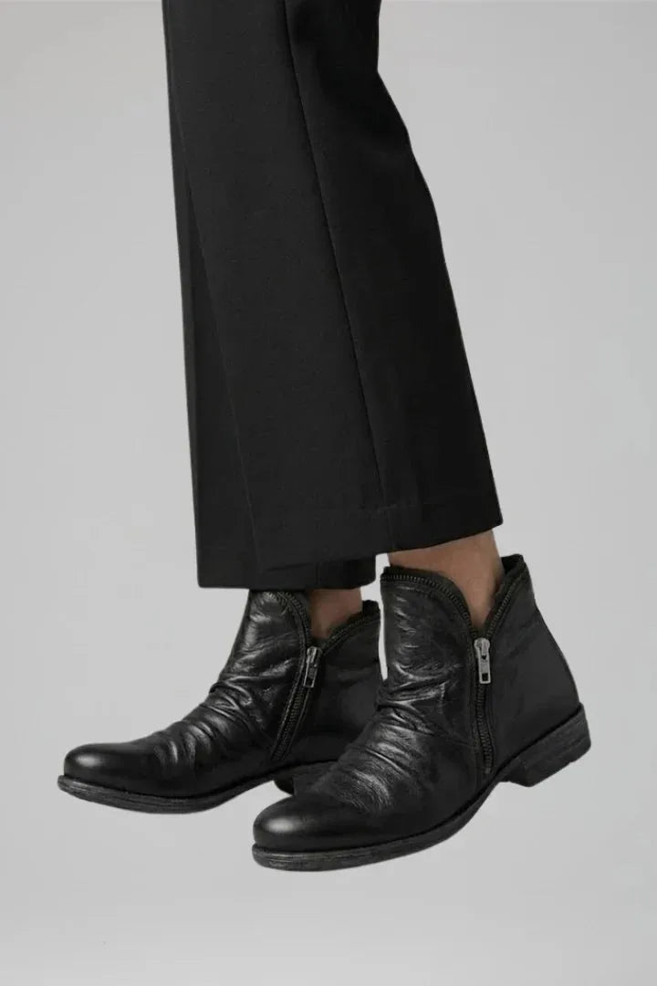 Three-quarter angle of black ruched ankle boots worn beneath cropped black trousers