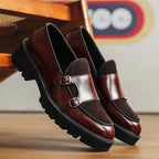 Side view of burgundy leather double monk-strap loafers with contrast dark suede panel, resting beneath a wooden chair