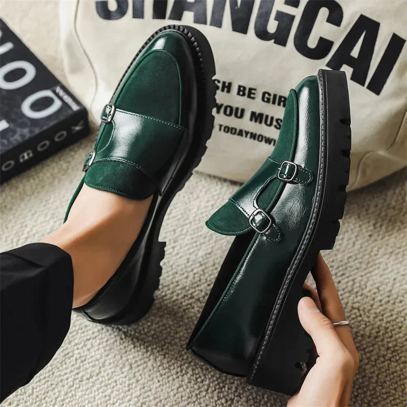 Close-up of green leather and suede double monk loafers held by hand, displaying the ridged black outsole